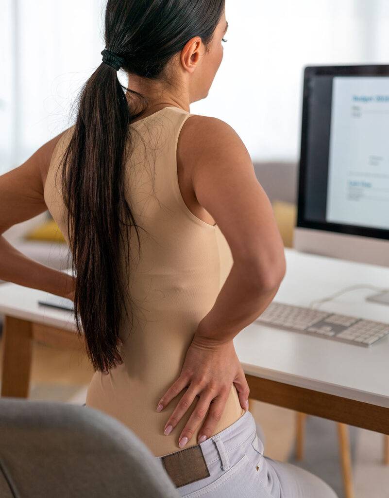 Patient with hands on hips in pain sitting at computer desk